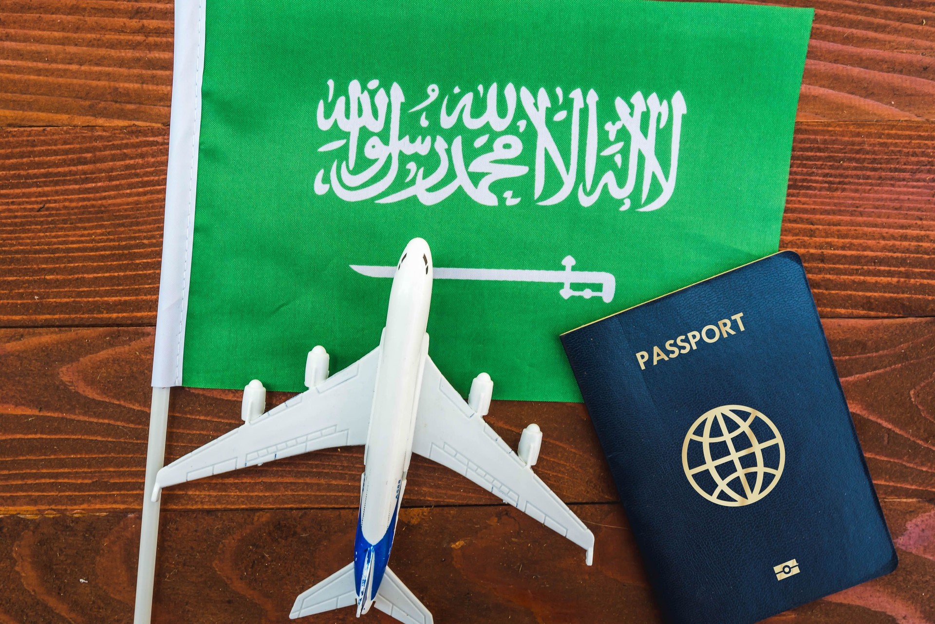 Flag of Saudi Arabia with passport and toy airplane on wooden background.